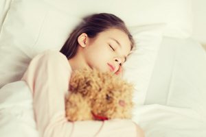 people, childhood, rest and comfort concept - girl sleeping with teddy bear toy in bed at home